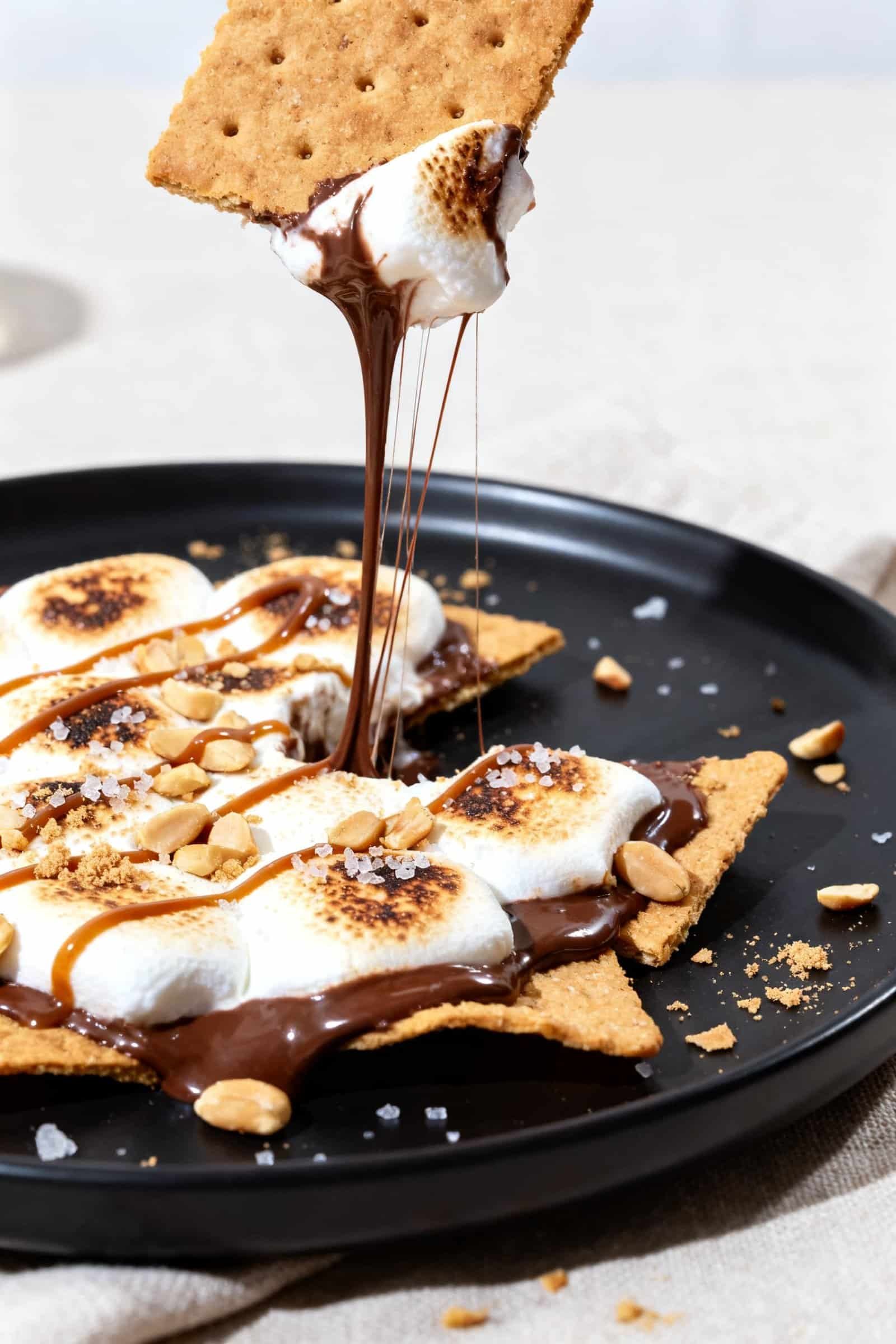 Extreme close-up detail of a plated portion of s’mores nachos on a matte black dessert plate: focu
